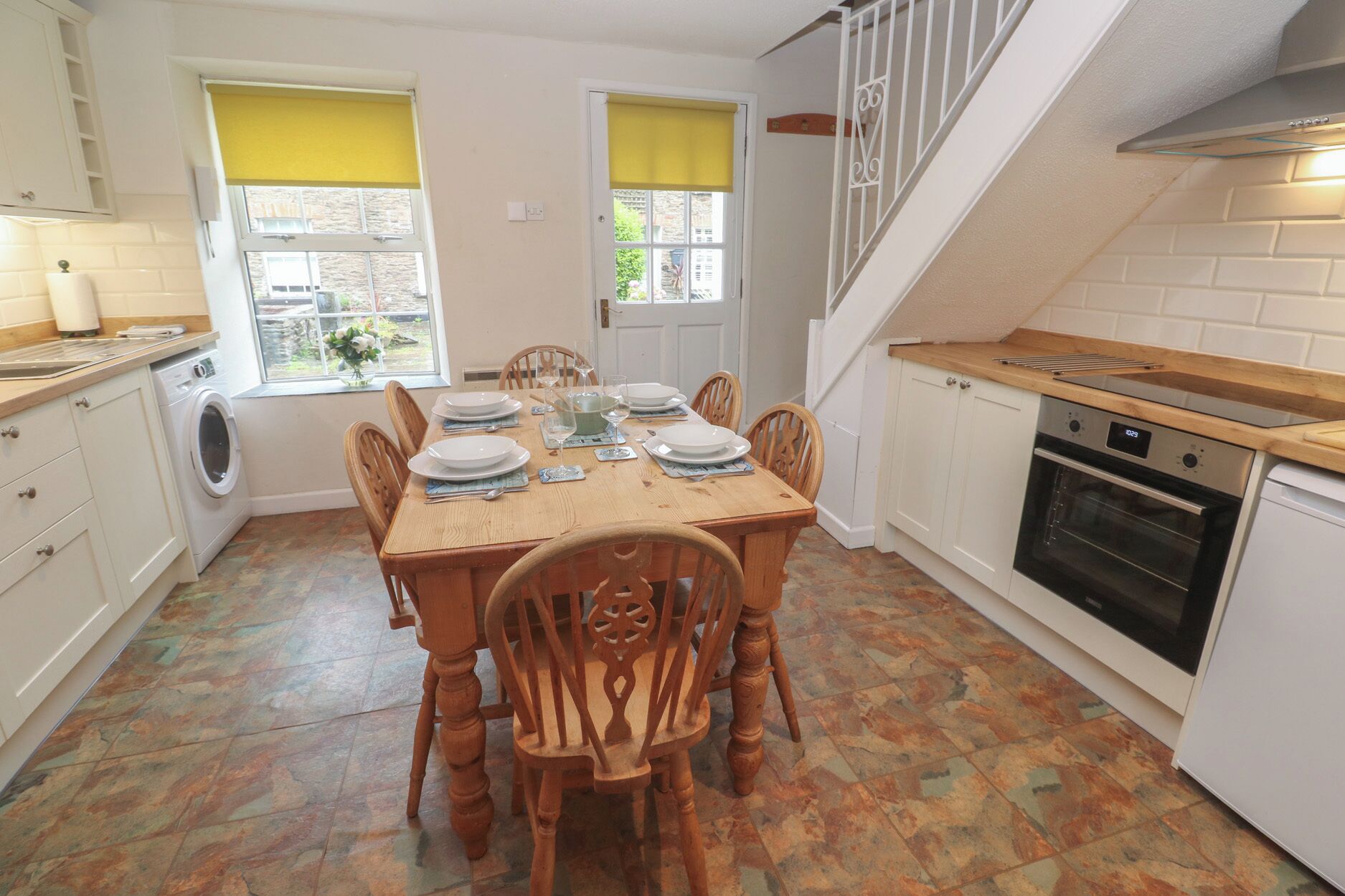 A compact kitchen with a dining area, a washing machine, and a staircase.