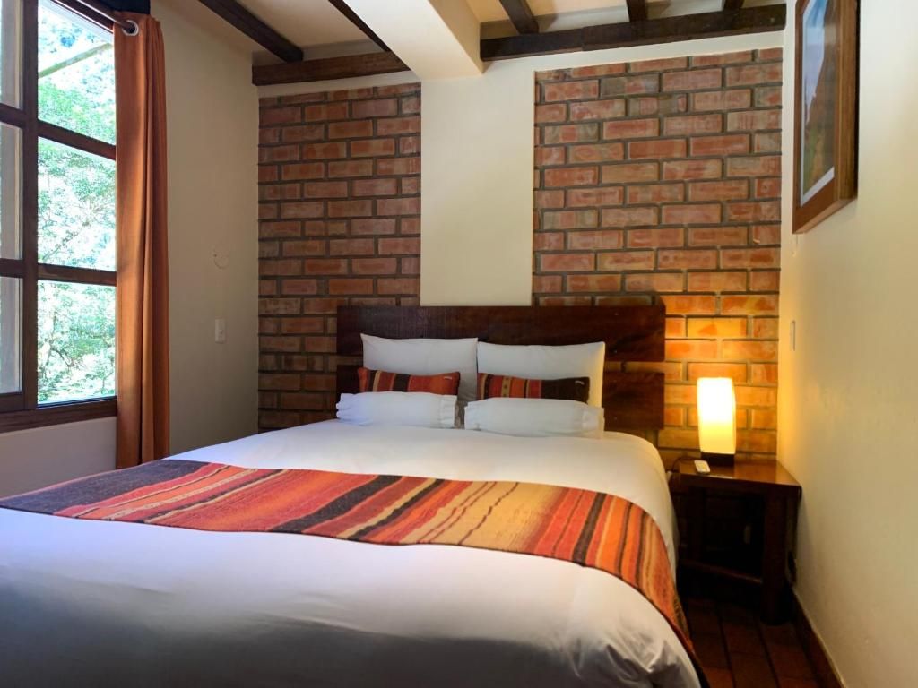 A bedroom with a brick wall, a bed with a striped blanket, and a bedside lamp.