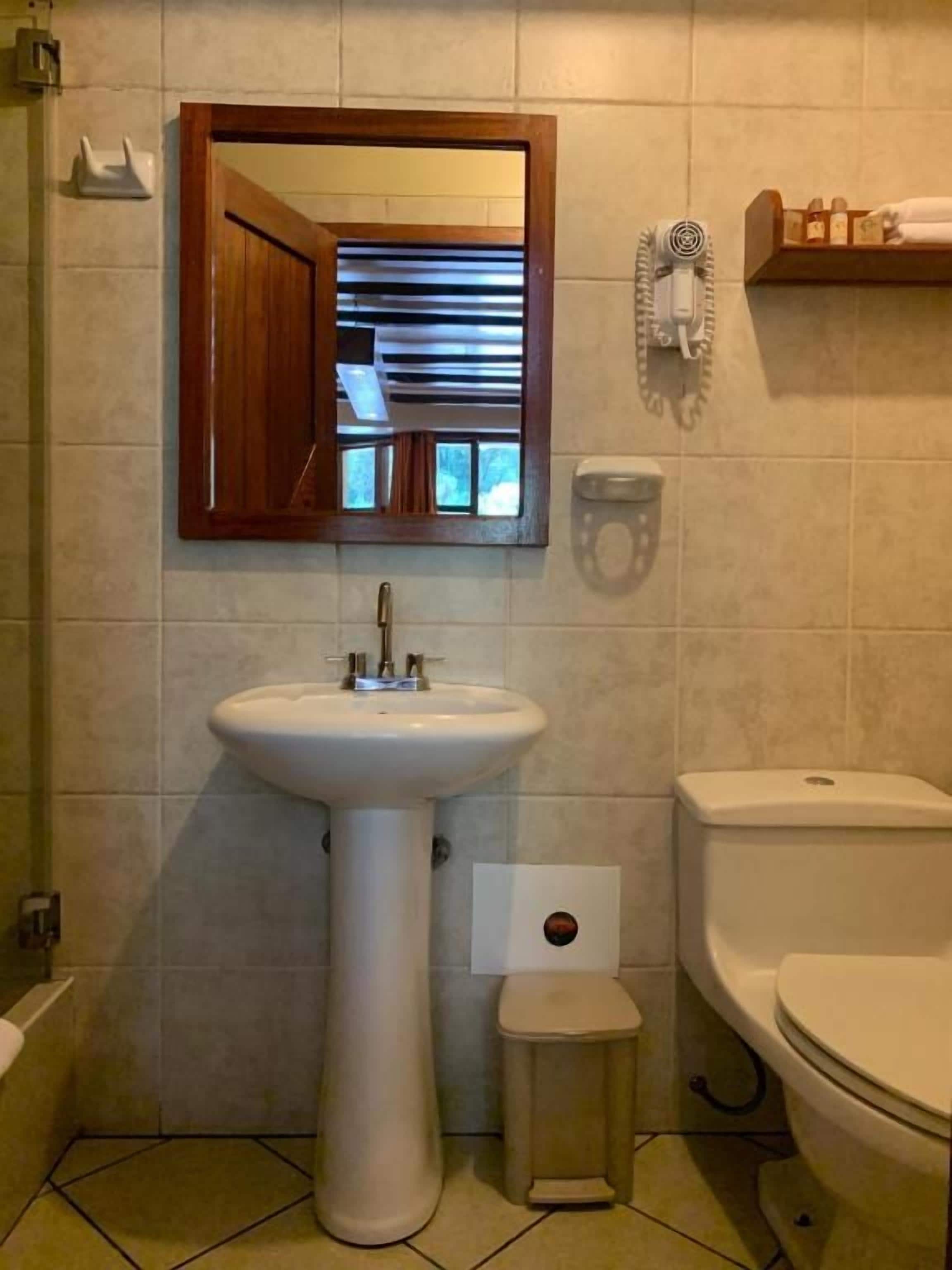 Un baño con lavamanos pedestal, inodoro y espejo con marco de madera.