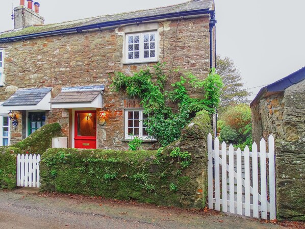 A stone building with a red door, white picket fence, and ivy growing on the walls. - 1 Gabberwell Cottages (Kingsbridge)