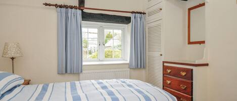 A bedroom with a bed, a window with curtains, a dresser, and a lamp.