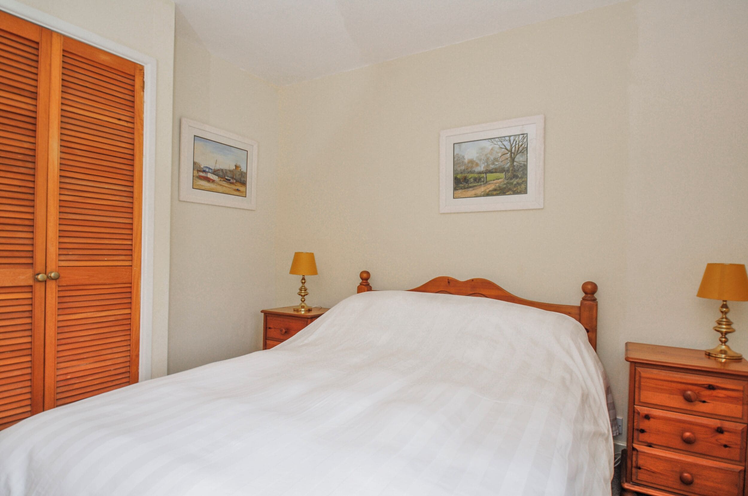 A bedroom with a bed, wooden nightstands, two lamps, and two framed pictures on the wall.