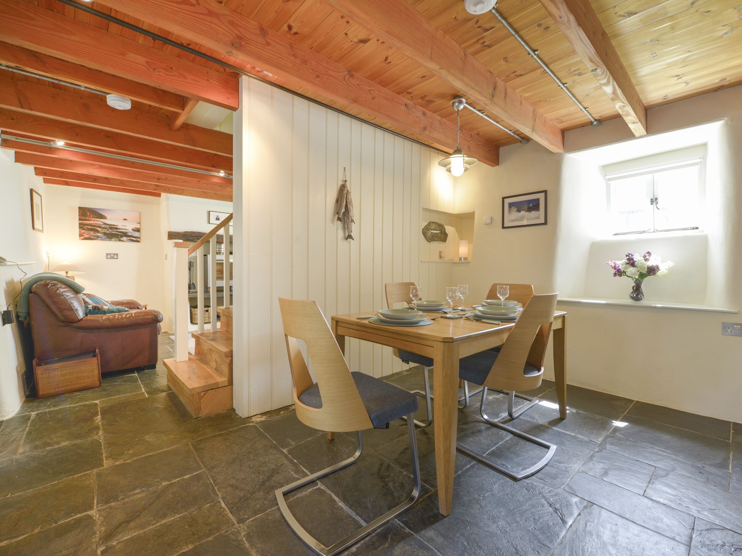 A dining area with a wooden table set for four, surrounded by chairs. A staircase leads to an upper level.