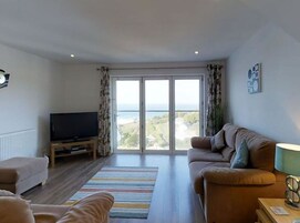 Una sala de estar con un ventanal grande, un televisor de pantalla plana, un sofá, una mesa de centro y un tapete a rayas.