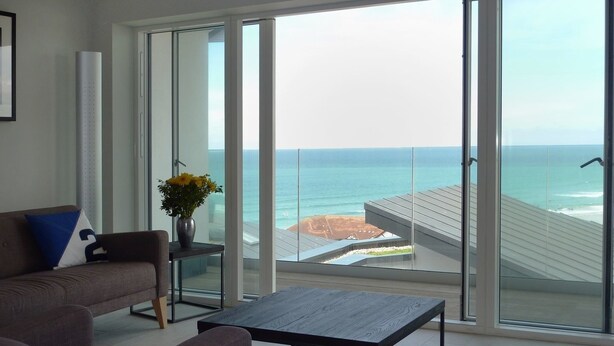 A modern living room with a sofa, a coffee table, and a view of the ocean through large glass doors. - Flat 8 Seascape (Newquay)