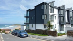 A modern multi-story residential building with a stone facade, large windows, and a view of the beach. - Flat 8 Seascape (Newquay)