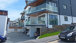 A modern multi-story residential building with a garage, a car parked in front, and a clear sky. - Flat 8 Seascape (Newquay)