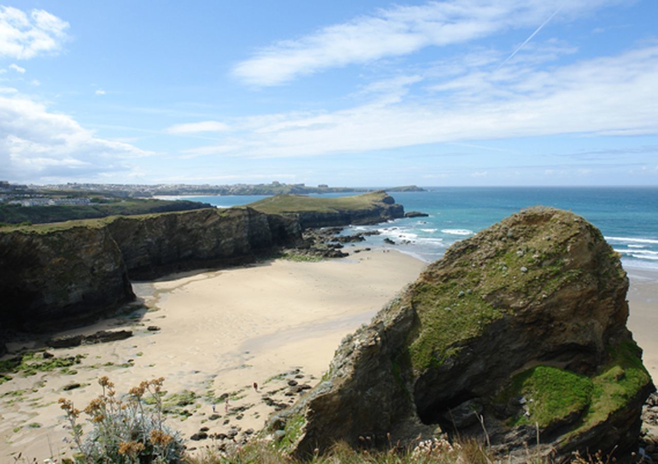 Um caminho costeiro com uma praia arenosa, falésias rochosas e o oceano.