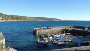 A harbor with boats docked at a stone pier, surrounded by calm water and a clear sky. - April Cottage (Helston)
