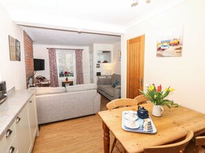 A compact living space with a kitchenette, a sofa, a dining table with a tray, and a TV in the background.