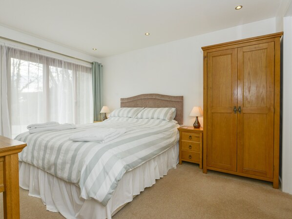 Une chambre à coucher comprenant un lit, des tables de chevet, une armoire et une fenêtre avec des rideaux.