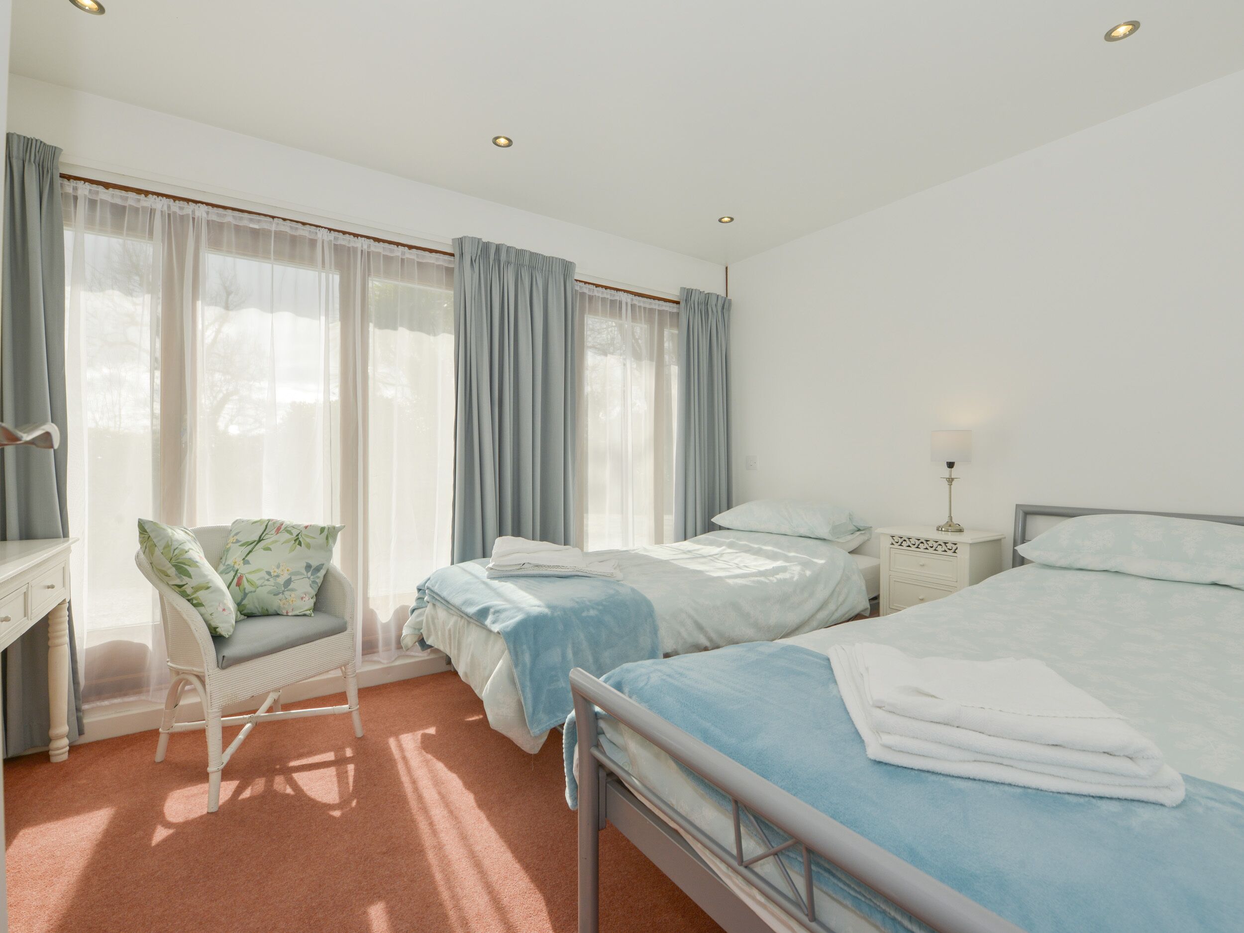 A hotel room with two beds, a chair, a desk, and a nightstand with a lamp.