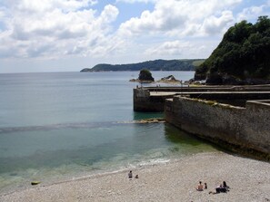 Une plage côtière avec une eau claire, un promontoire rocheux et un mur de pierres.