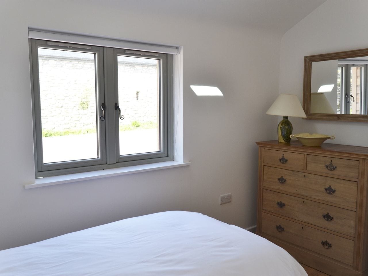 A bedroom with a bed, a dresser, a window, and a mirror.
