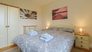 Un dormitorio con cama, mesita de noche, cómoda y dos cuadros en la pared.