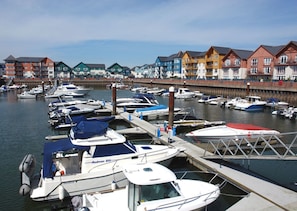 A marina with several boats docked, a wooden pier, and colorful buildings in the background.