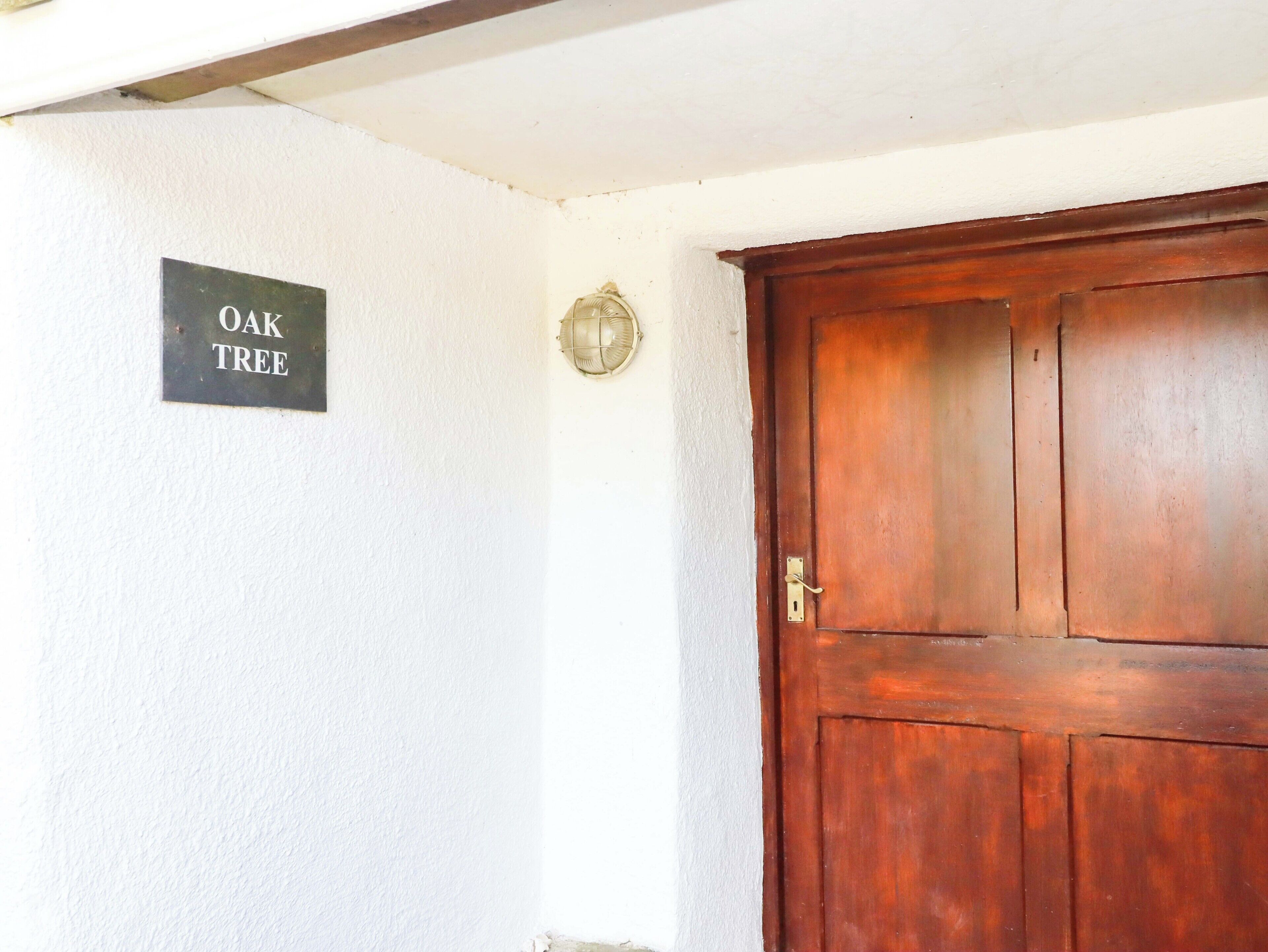 Une porte en bois avec une poignée en laiton, un heurtoir en laiton et une enseigne portant l’inscription « CHÊNE » sur le mur.
