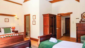 A bedroom with two beds, wooden furniture, a chandelier, and a view of the bathroom.