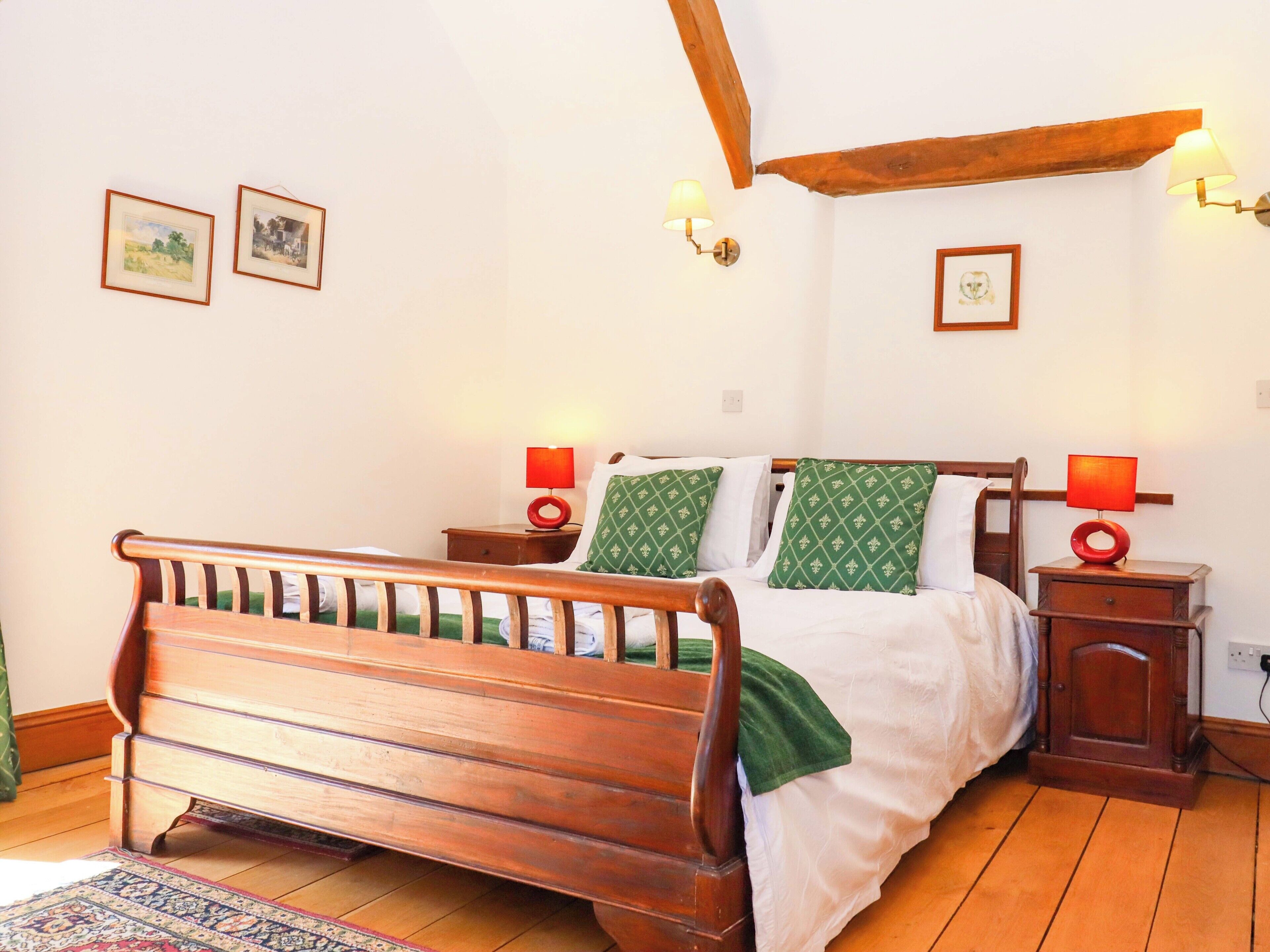 A wooden bed with a headboard, two bedside tables with lamps, and a wall with framed pictures.