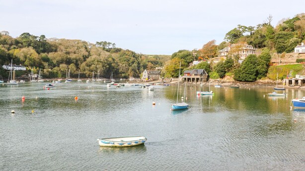 A harbor with boats, a small boat in the foreground, and buildings on the hillside. - Junket Cottage (Plymouth)