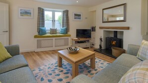 A cozy living room with a sofa, a coffee table, a fireplace, and a television. - Junket Cottage (Plymouth)