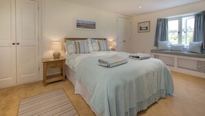 A bedroom with a bed, bedside tables, a window with curtains, and a view of the outdoors. - Junket Cottage (Plymouth)