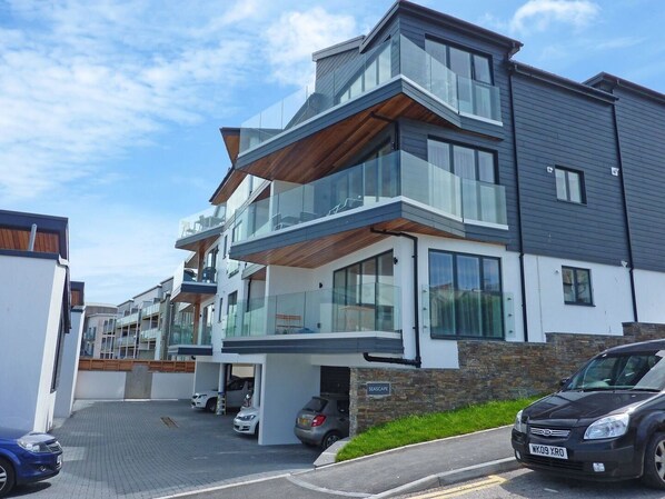 A modern multi-story residential building with a garage and a car parked in front.