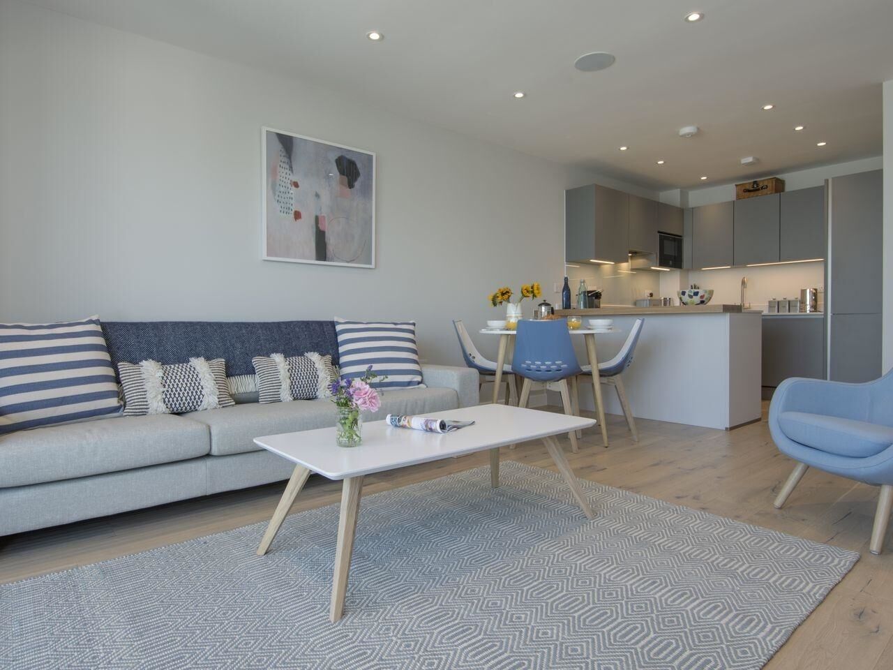 A modern living room with a sofa, coffee table, and chairs. There is a kitchen area in the background.