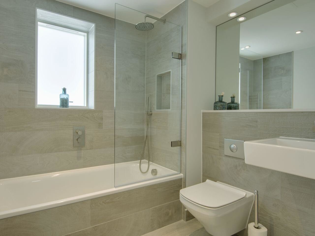 A modern bathroom with a glass-enclosed shower, a white bathtub, and a toilet.