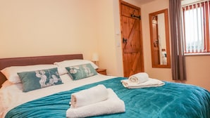 Ein ordentlich gemachtes Bett mit einer türkisfarbenen Tagesdecke, zwei Kissen und zwei aufgerollten Handtüchern.