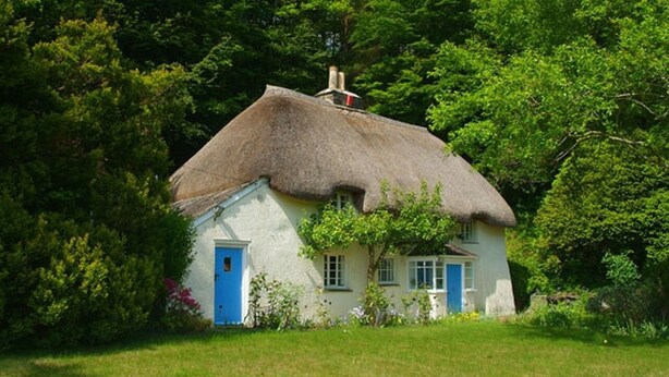 A thatched-roof cottage with a blue door and windows, surrounded by lush greenery. - Lew Quarry Cottage (Okehampton)