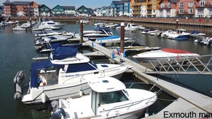 A marina with several boats docked, a wooden pier, and colorful buildings in the background. - Grooms Cottage (Exeter)