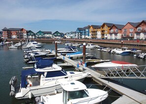 A marina with several boats docked, a wooden pier, and colorful buildings in the background.