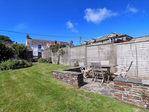 A backyard with a stone wall, a wooden table, and two chairs. - Agar Cottage (Port Isaac)