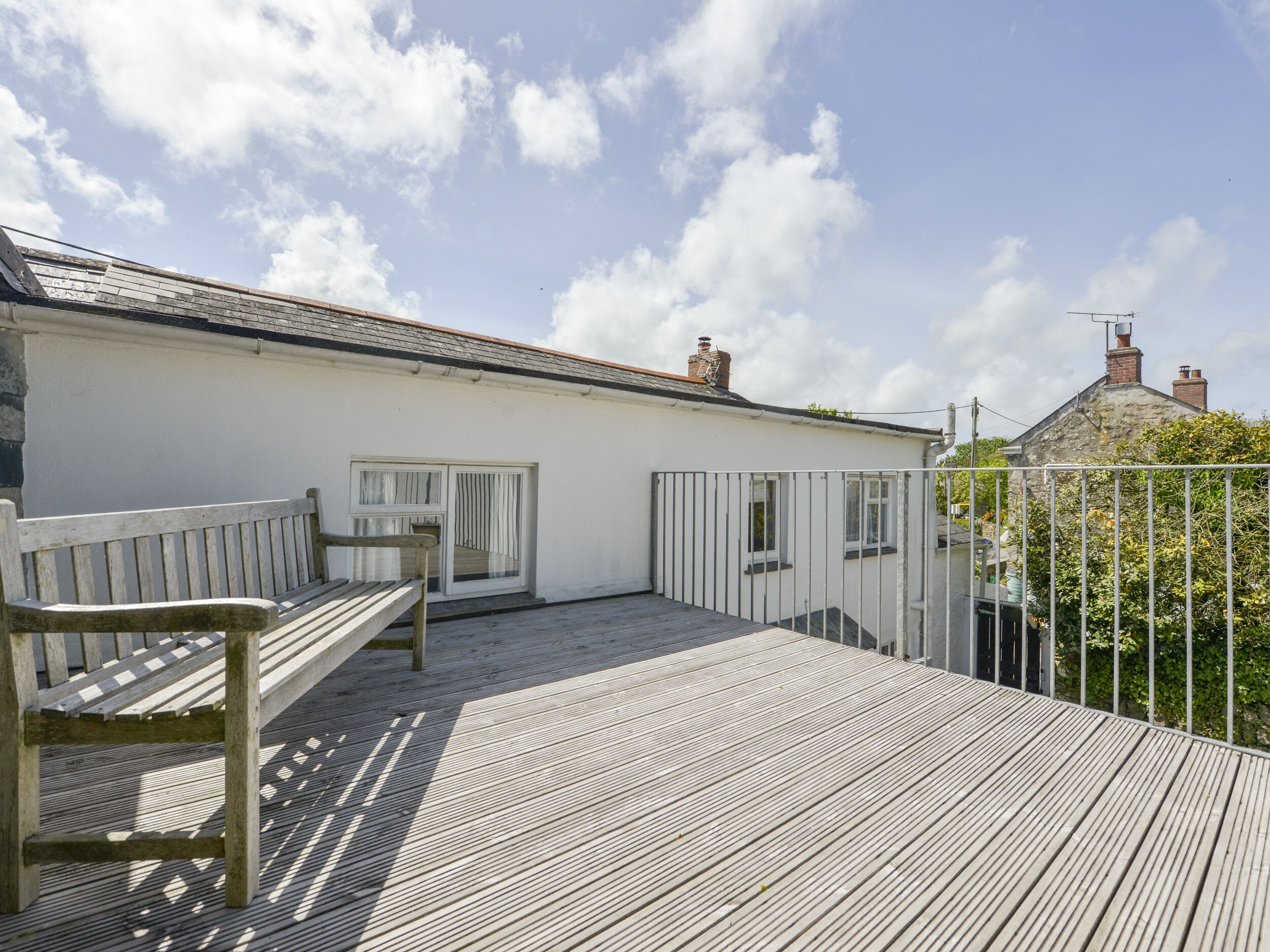A wooden deck with a bench, a white building with a door and windows, and a metal fence.