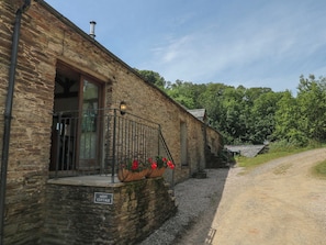 A stone building with a sign reading 'MIXIT COTTAGE,' a gravel path, and a forested area in the background.