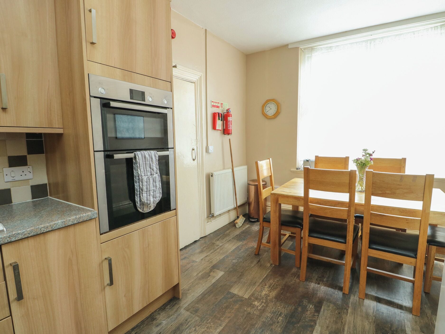 A kitchen with wooden cabinets, a built-in oven, a dining table with chairs, and a window with a view.