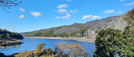 Un paisaje montañoso con cielo azul despejado, terreno rocoso y una masa de agua tranquila.