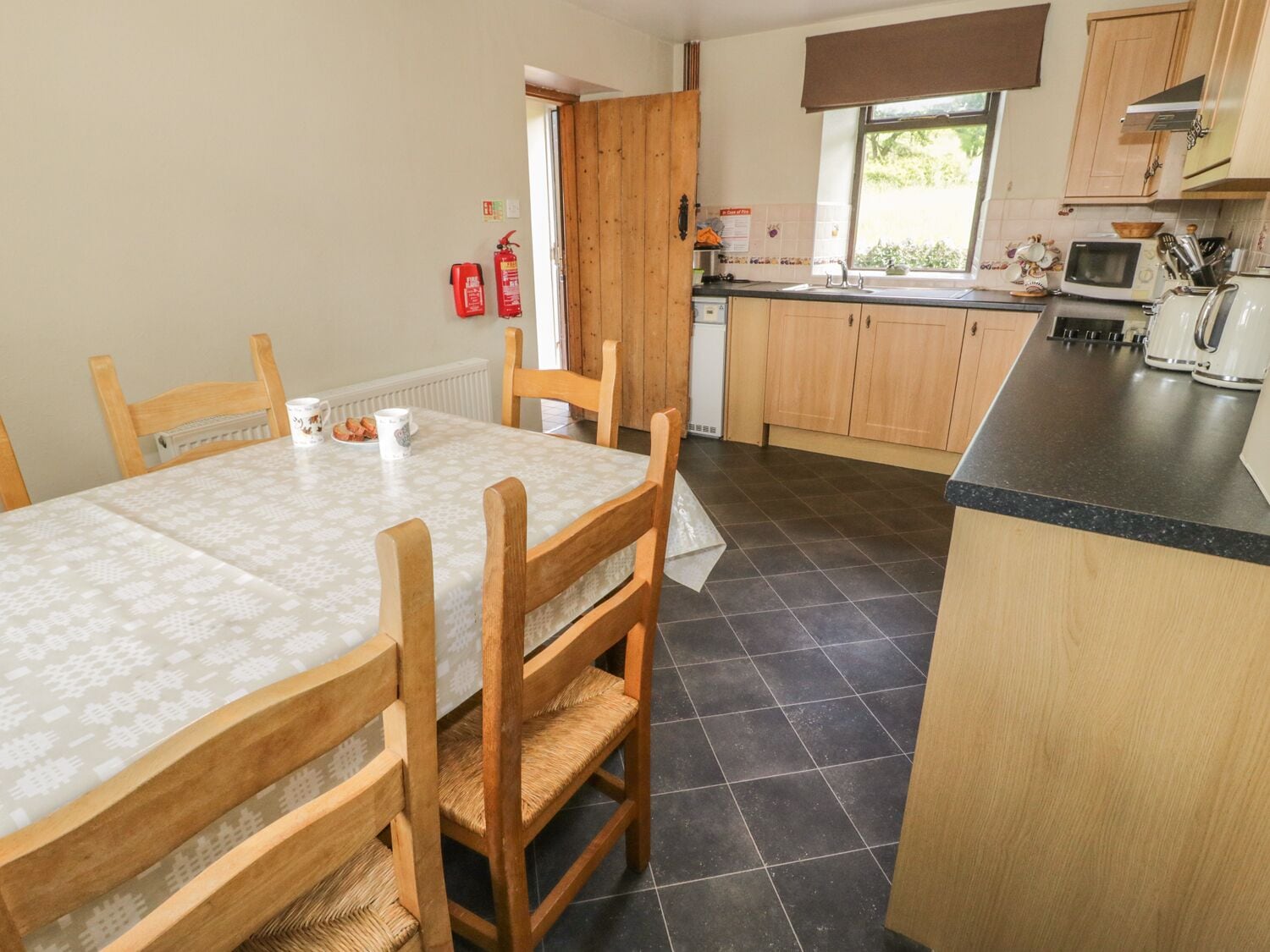 A kitchen with wooden cabinets, a tiled floor, a dining table with chairs, and a window.