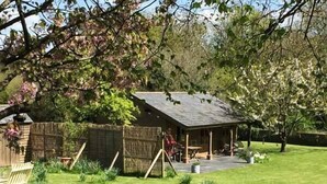 A rustic wooden cottage with a sloped roof, surrounded by a well-maintained lawn and a wooden fence. - The Springs (Ryde)
