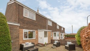 Une maison à deux étages, construite en briques, dotée d’un patio aménagé avec du mobilier d’extérieur et un petit jardin.