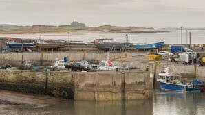 Un port où sont amarrés des bateaux, un château en arrière-plan et une plage de sable.