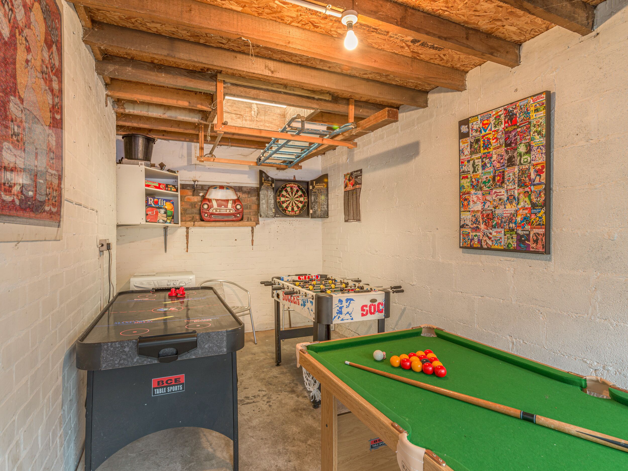 Une pièce équipée d’une table de billard, d’un baby-foot, d’un jeu de fléchettes et ornée de divers posters sur les murs.