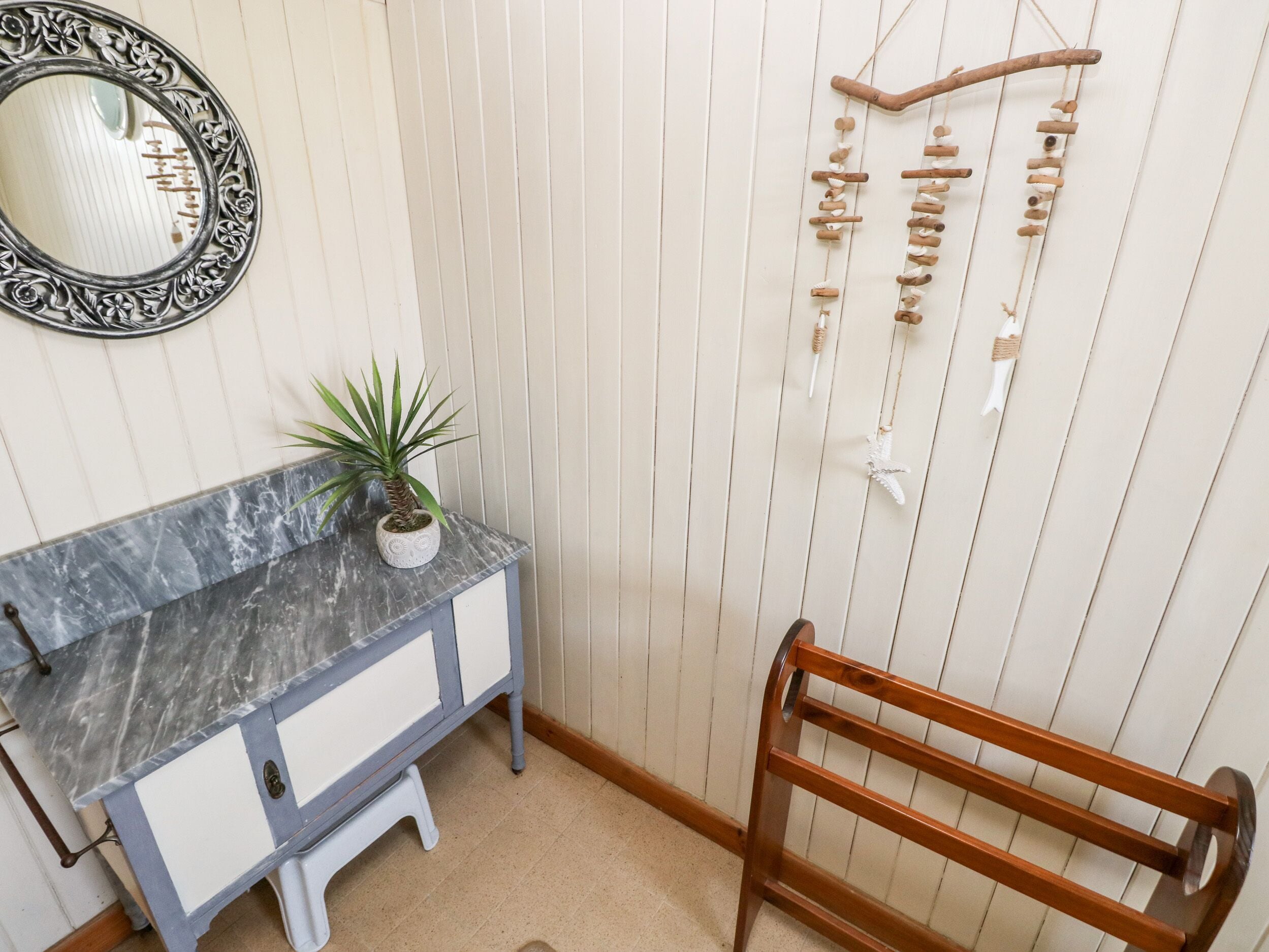 A bathroom with a marble vanity, a potted plant, a hanging ornament, and a wooden chair.