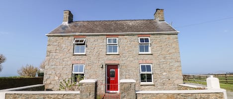 A stone house with a red door, multiple windows, and a chimney.
