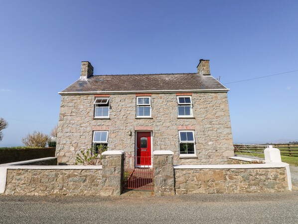 A stone house with a red door, multiple windows, and a chimney.