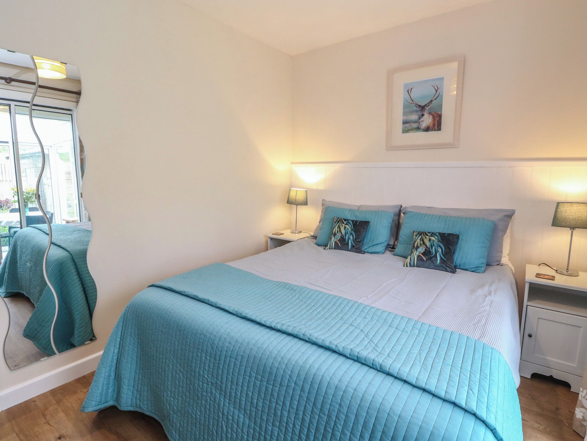 A bedroom with a large bed, two bedside tables with lamps, a framed picture on the wall, and a window with a view.