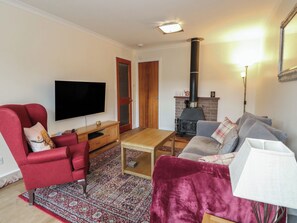 Uma sala de estar com televisão, lareira, sofá e uma poltrona vermelha.