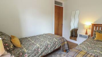 Un dormitorio con dos camas, una puerta de madera, un espejo, una mesita de noche y una mesita auxiliar.