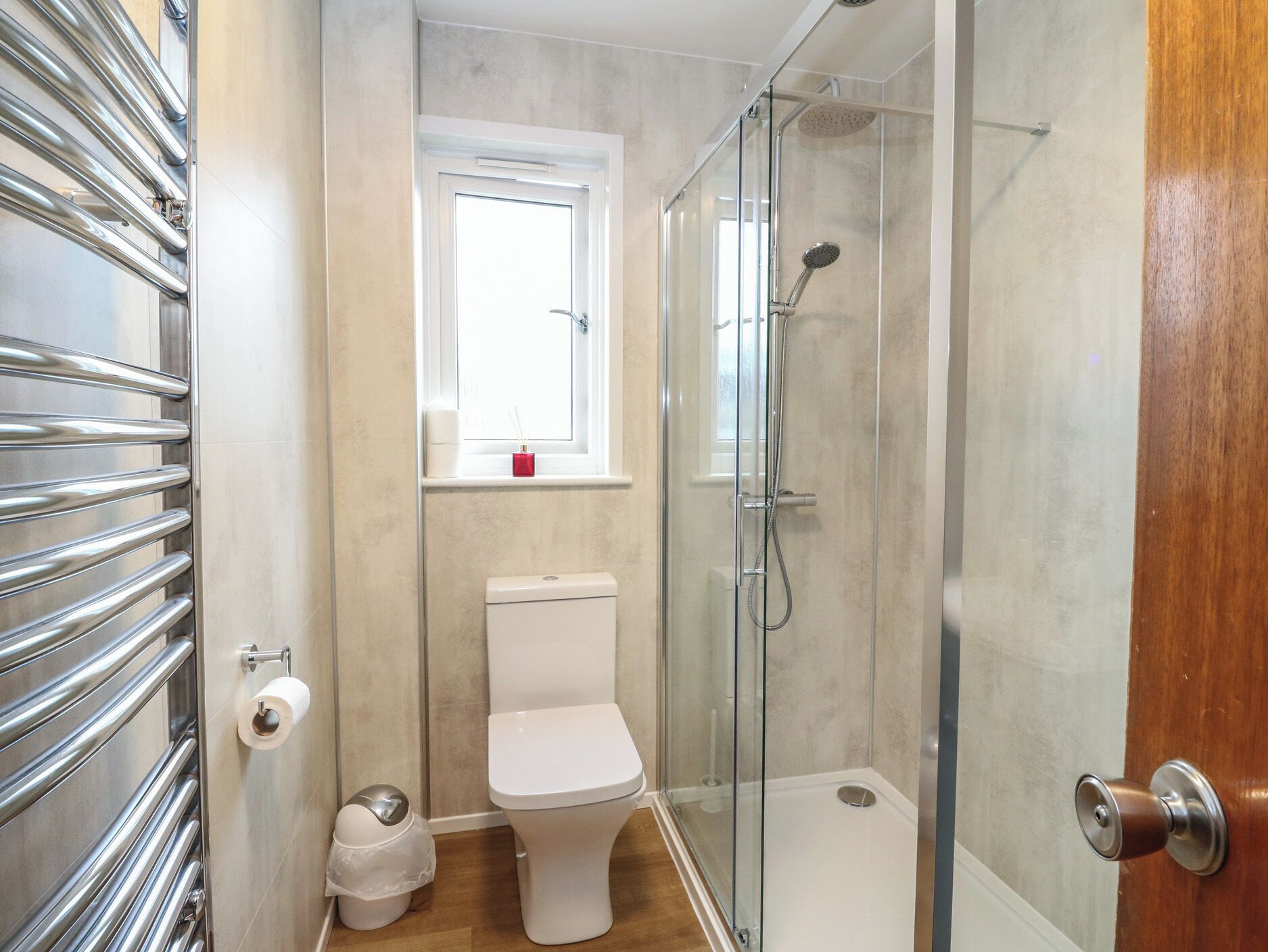 A bathroom with a glass-enclosed shower, a toilet, a bidet, and a window with a red object on the sill.